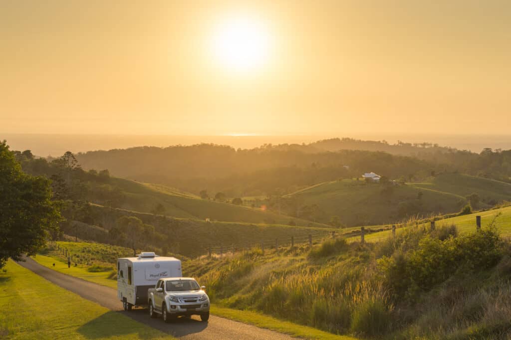 Car towing caravan down a road at sunset